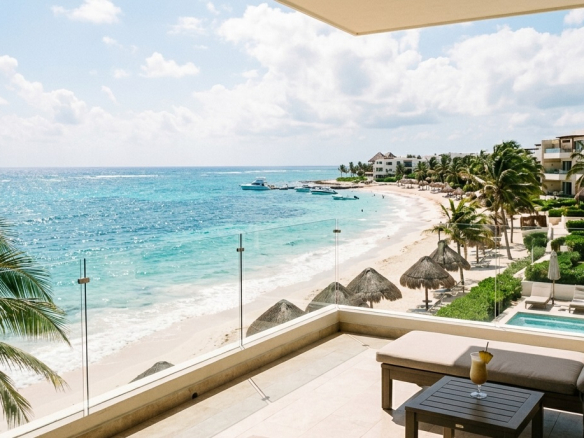 An ocean-view balcony and private terrace of luxurious, contemporary Akumal beachfront condos for sale, featuring high-rise buildings, comfortable lounge chairs, and direct beach access.